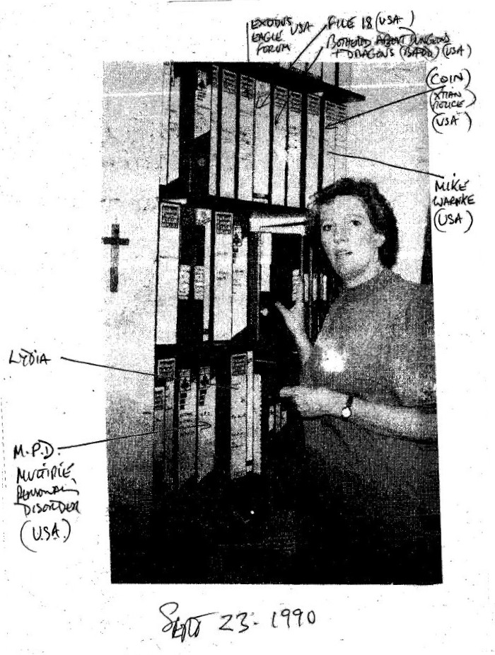 Maureen Davies in front of her bookshelf
                      showing propaganda from the USA on SRA